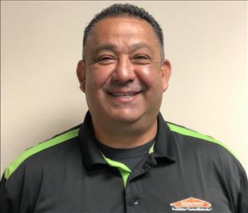 Male employee dressed in SERVPRO uniform in front of a tan wall smiling at the camera.